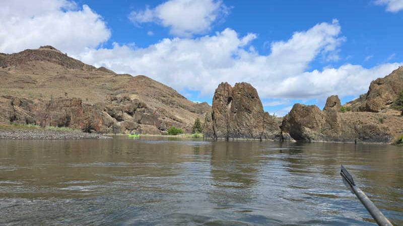 John Day River scene with rocky cliffs and mountains under a blue sky with clouds.