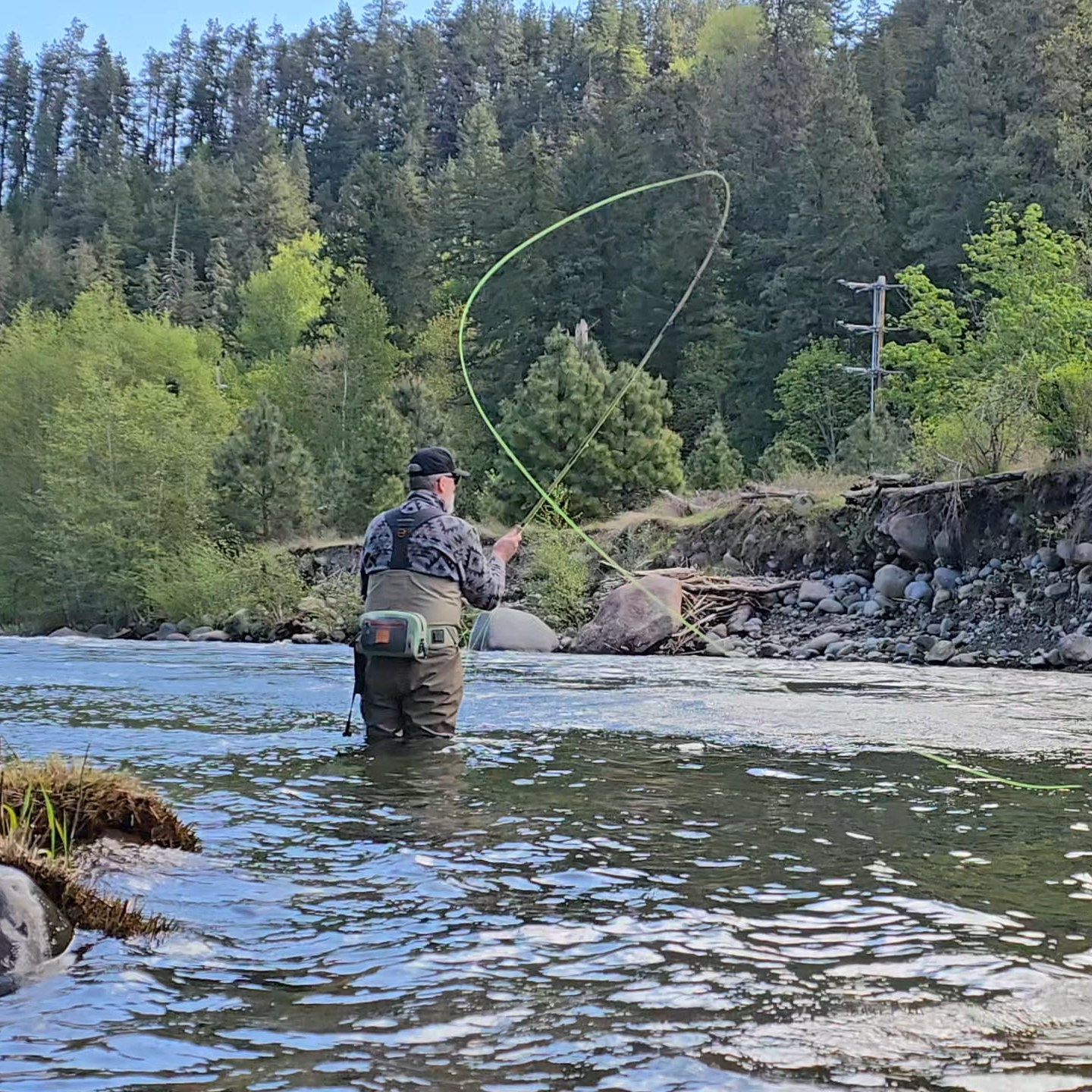 John spey casting in a river with trees and rocks in the background