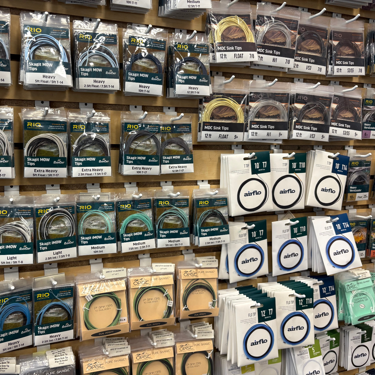 Display of fishing spey line packages on a wooden rack with visible brand logos - RIO, airflo, OPST