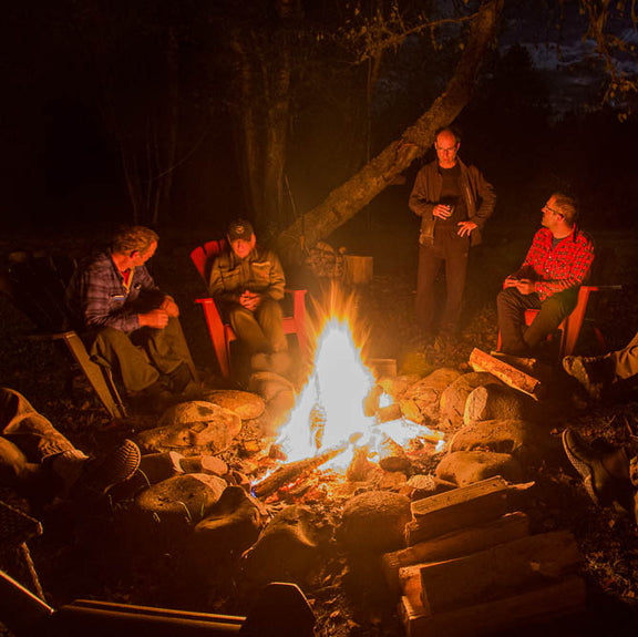 Group of anglers gathered around a campfire on steelhead trip near a river