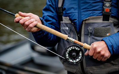 Angler holding a spey fishing rod, reel and line - wearing Simms waders with a blurred background