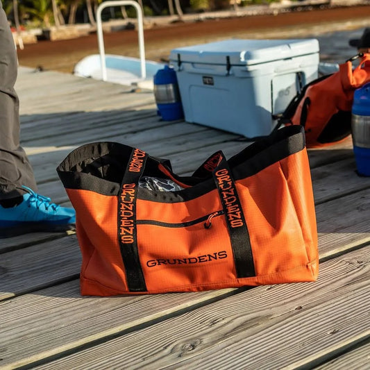 Orange tote bag with black accents on a wooden dock, featuring the 'Grundens' brand.